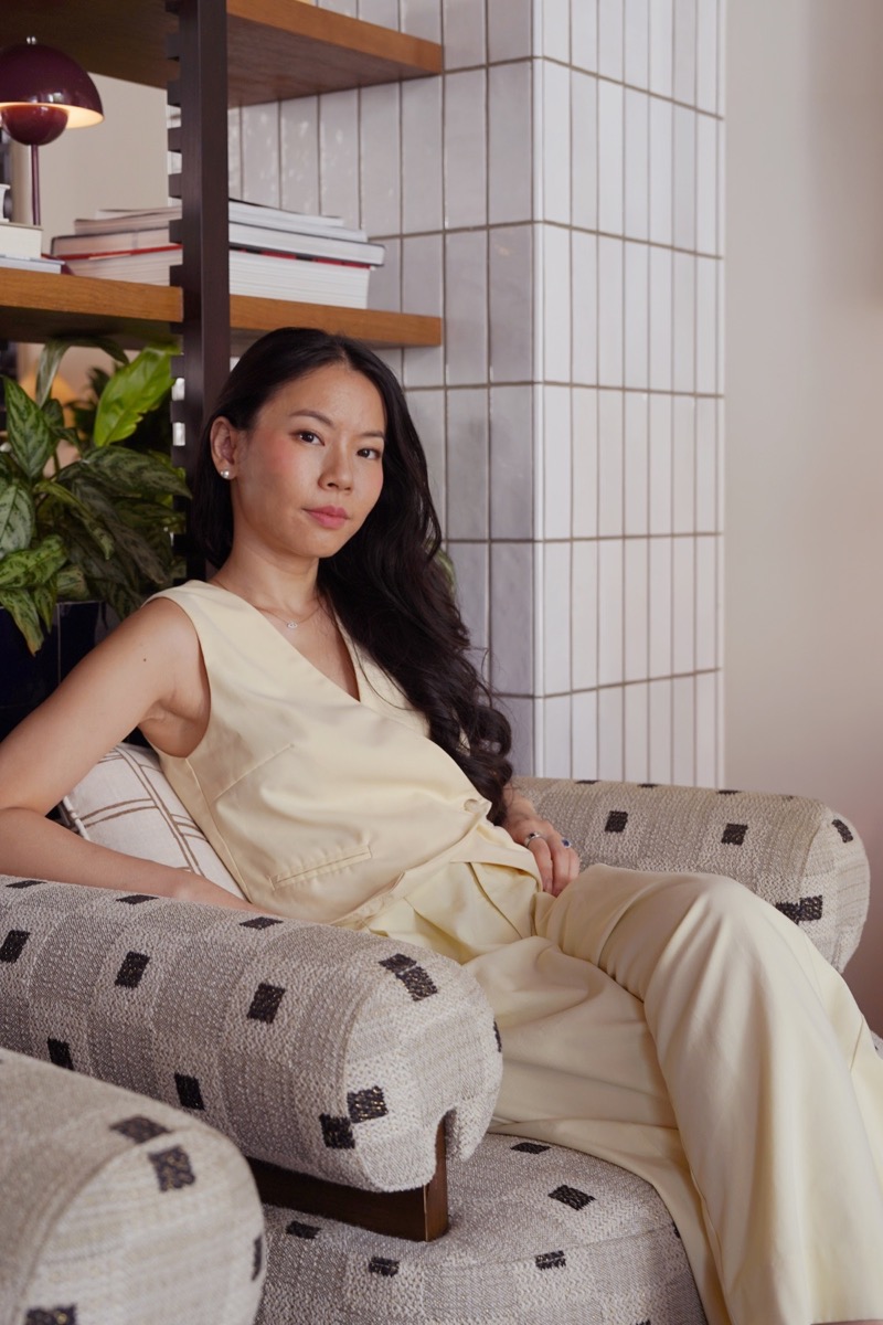 Christine Tan sitting in a patterned armchair in front of a bookshelf